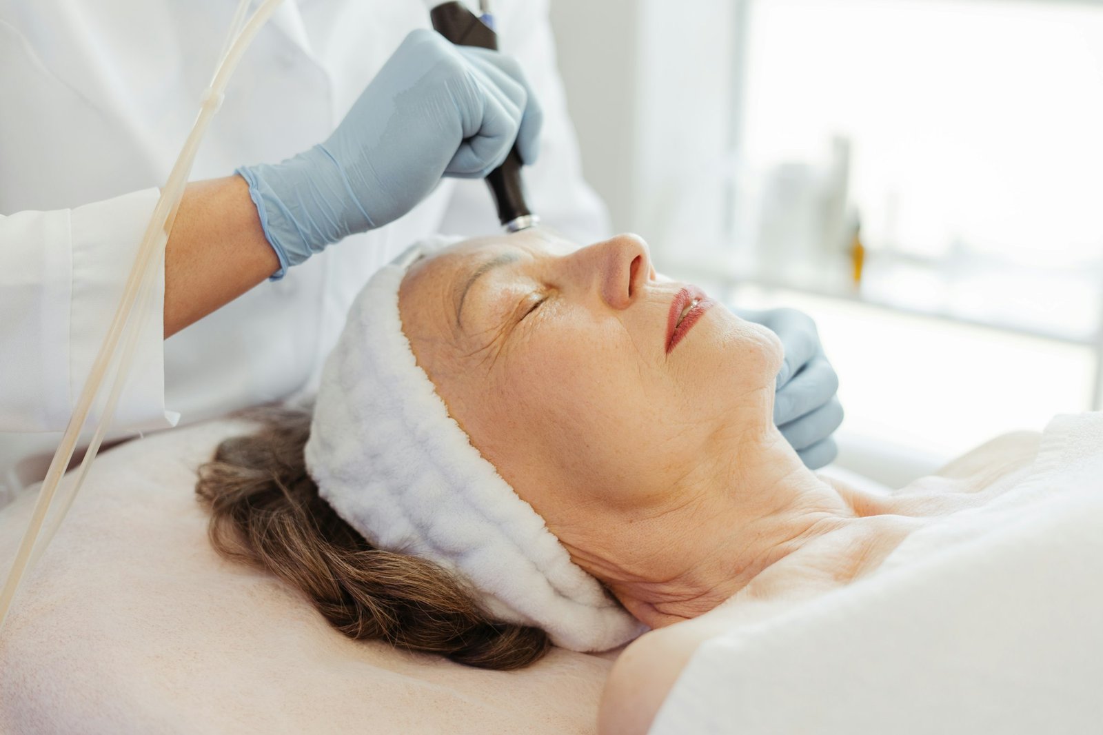 Beautician in gloves conducts vacuum cleaning and polishing face skin of senior, mature woman